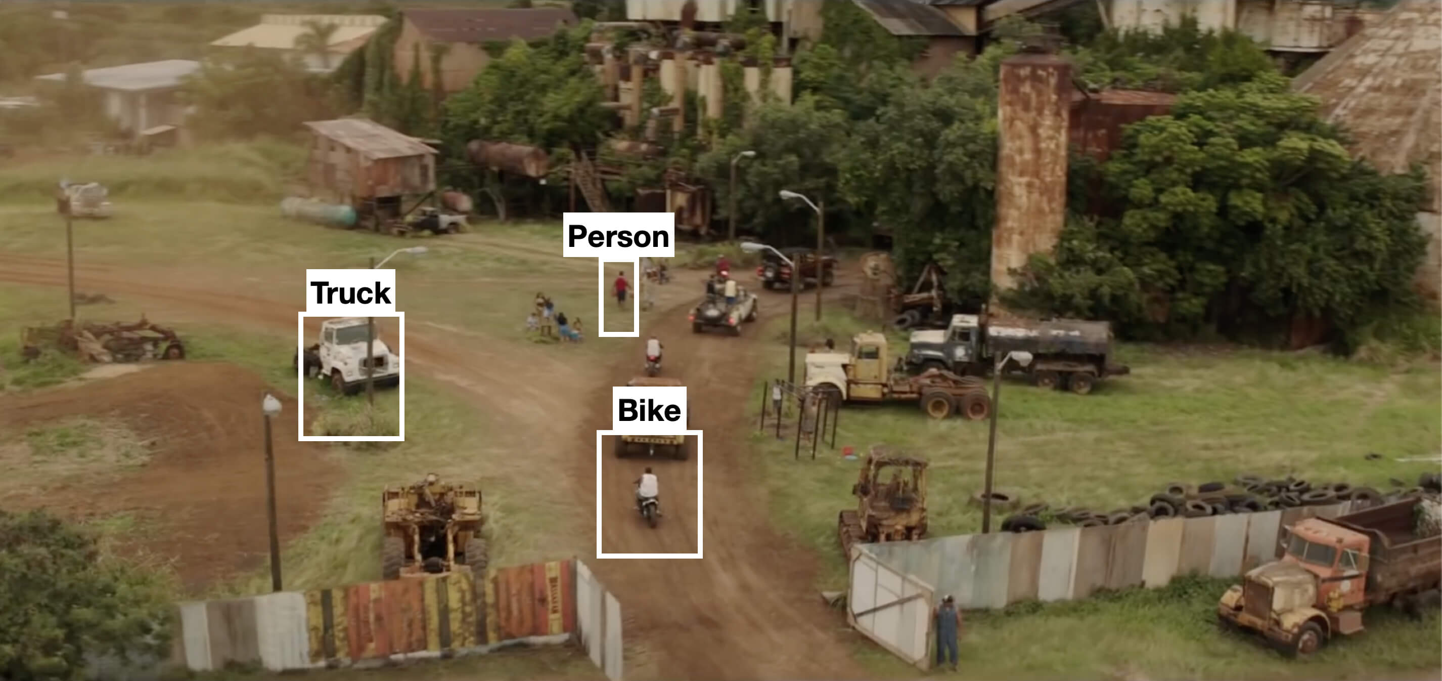 Video frame of a dusty village street with a truck, a person and a bike outlined by detection boxes
